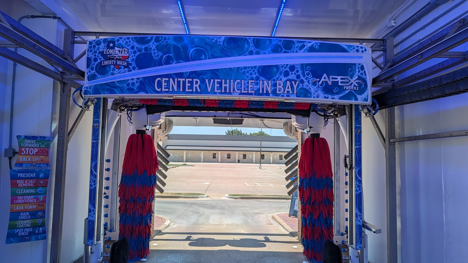 Inside Bay 1 at Lone Star Liberty Wash in Granbury — the Wash World Profile Apex gantry lit in blue, with the ChemQuest wash-step list on the bay wall